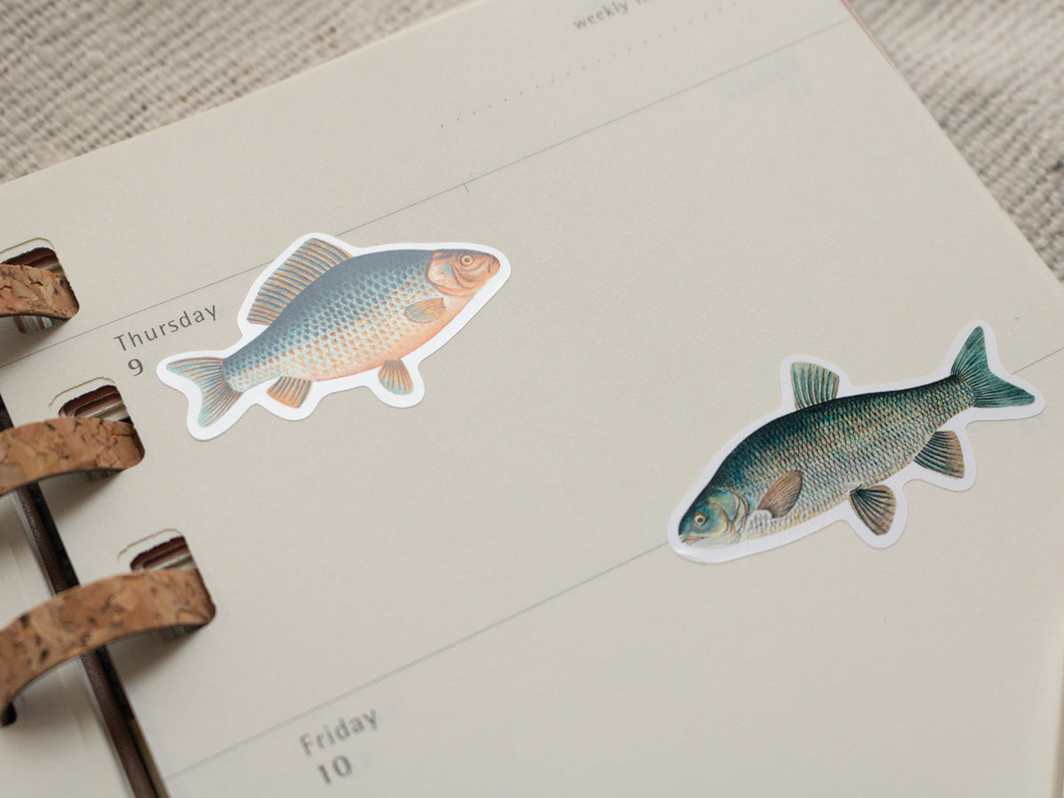 Two fish stickers on a planner page with a textured surface.