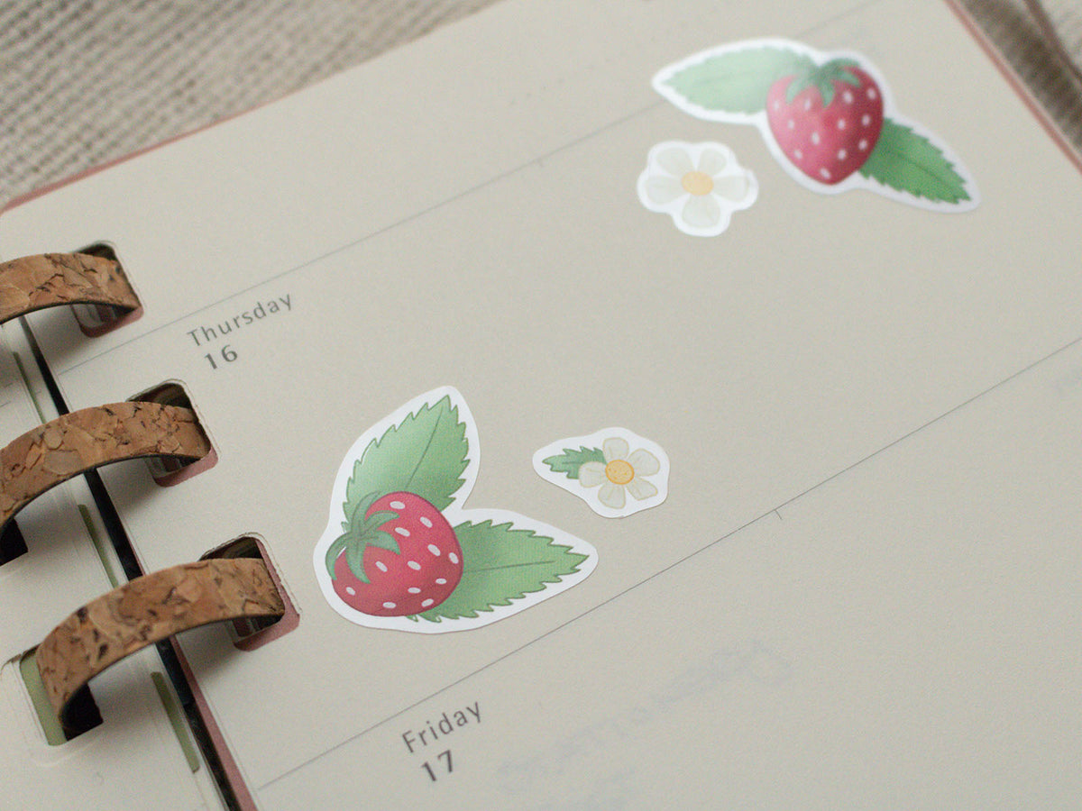 Stickers of strawberries and flowers on a planner page.