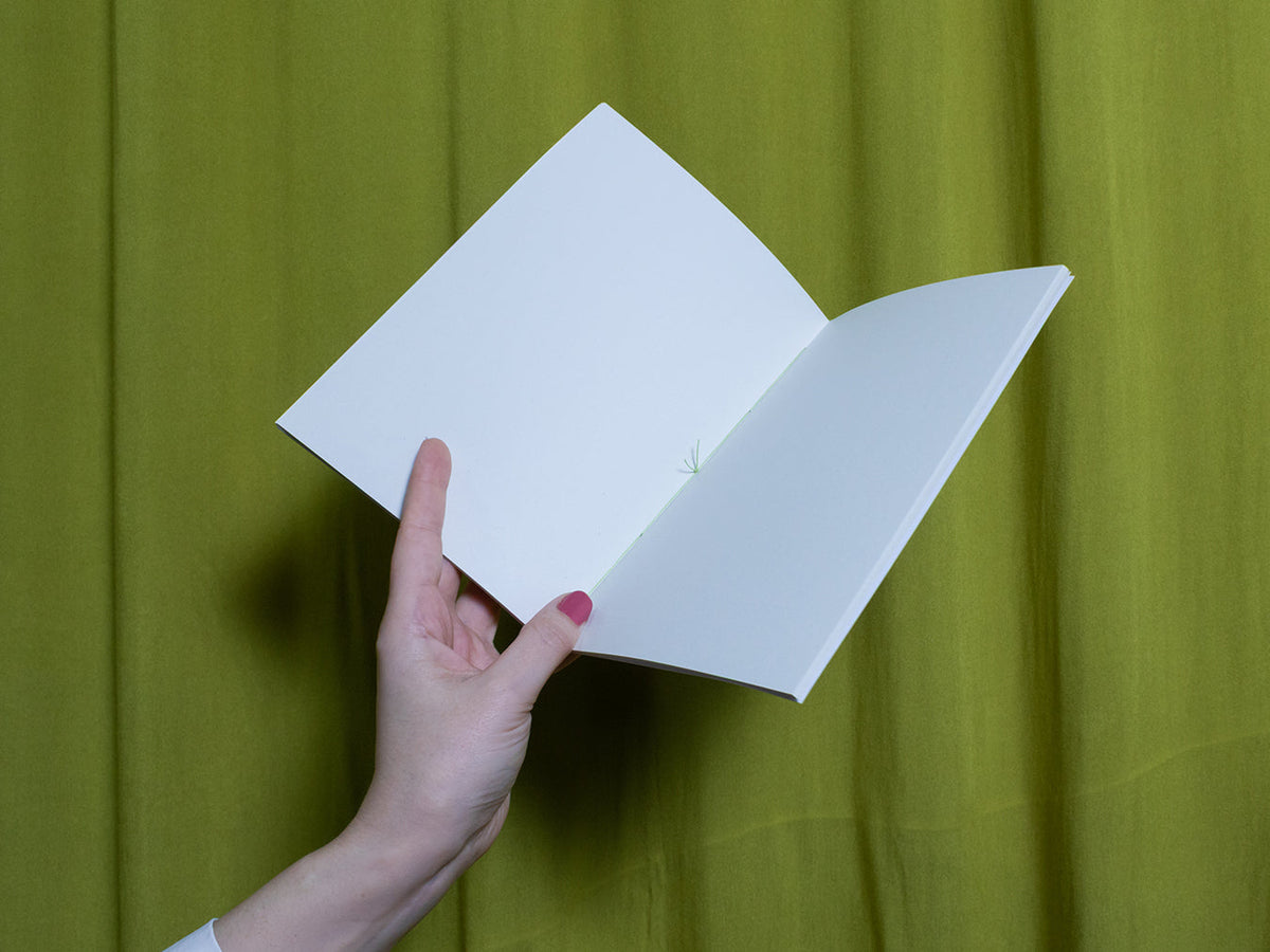 Hand holding an open blank sketchbook against a green curtain background