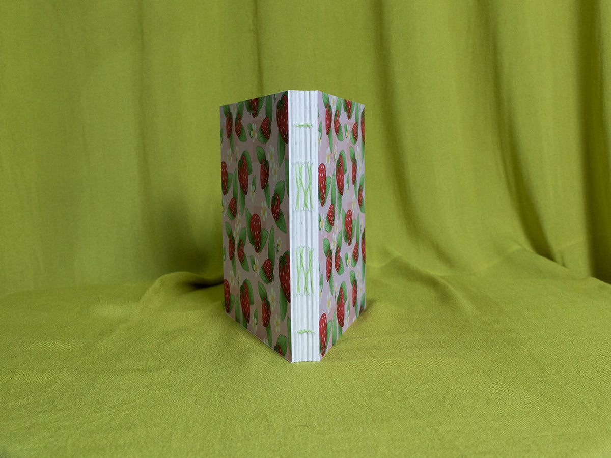 Open spine sketchbook with strawberry pattern on a green fabric background