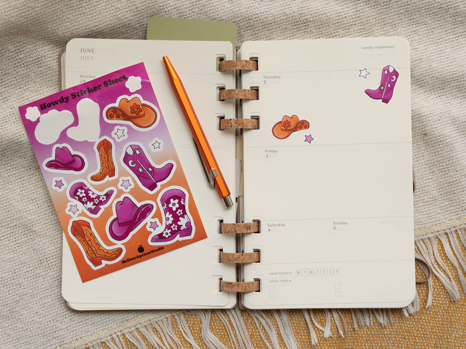 Open planner with cowboy-themed stickers and a pen on a textured surface