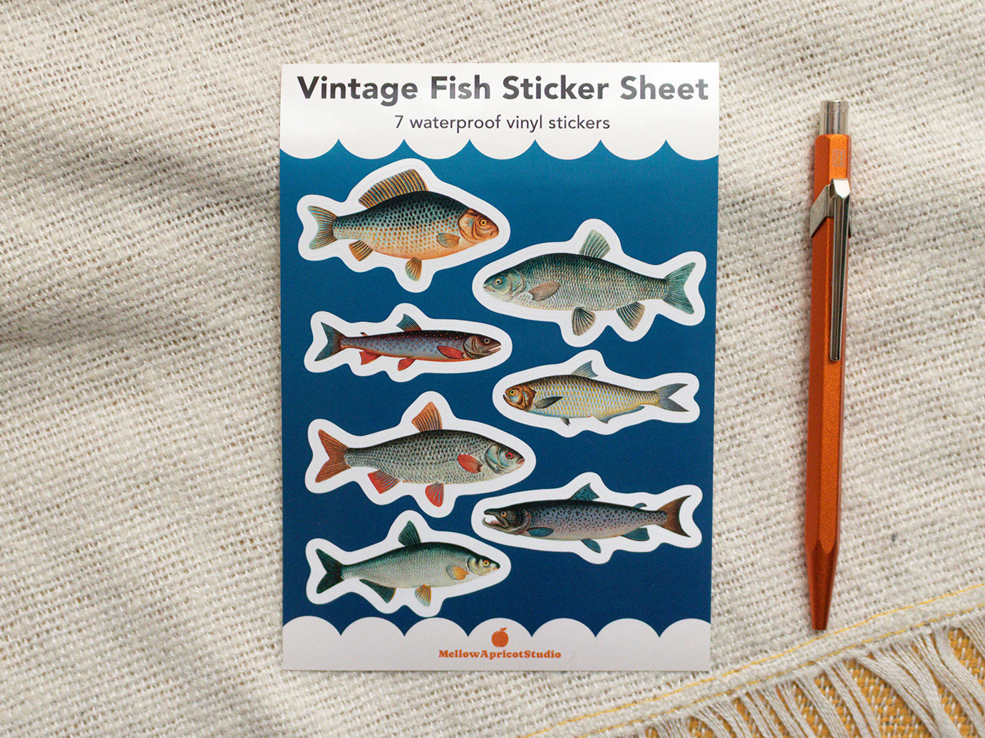 Vintage fish sticker sheet with seven waterproof vinyl stickers on a textured surface with a pen.