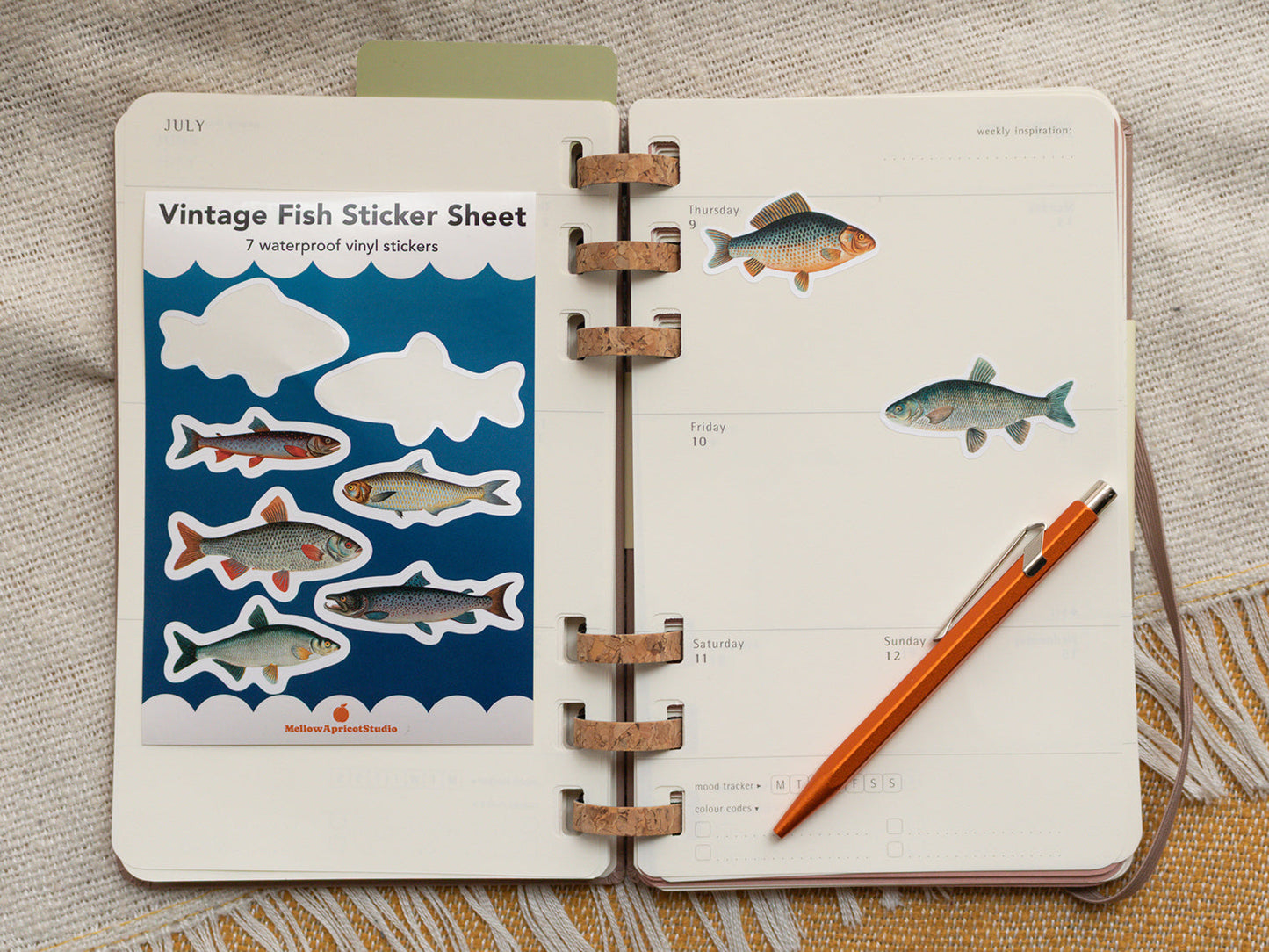 Open planner with vintage fish stickers and a pen on a textured surface