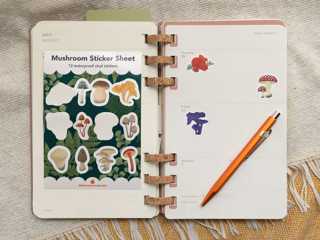 Open planner with mushroom stickers and a pencil on a textured surface