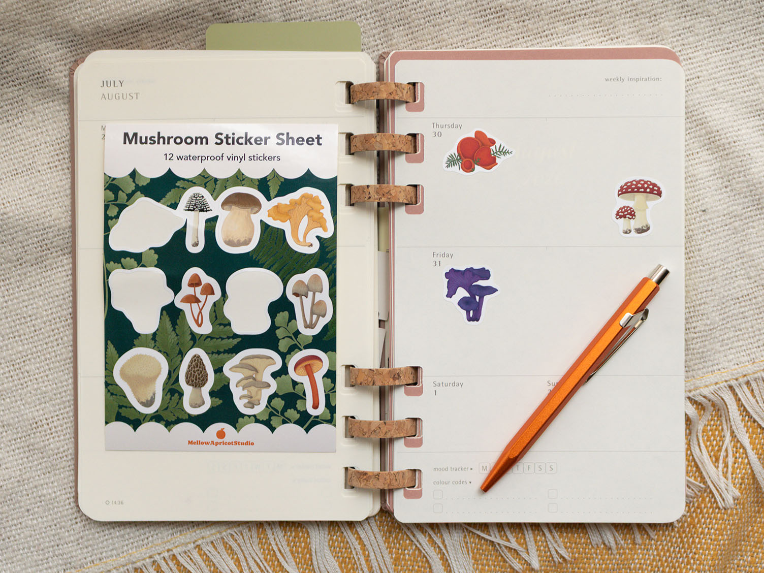 Open planner with mushroom stickers and a pencil on a textured surface