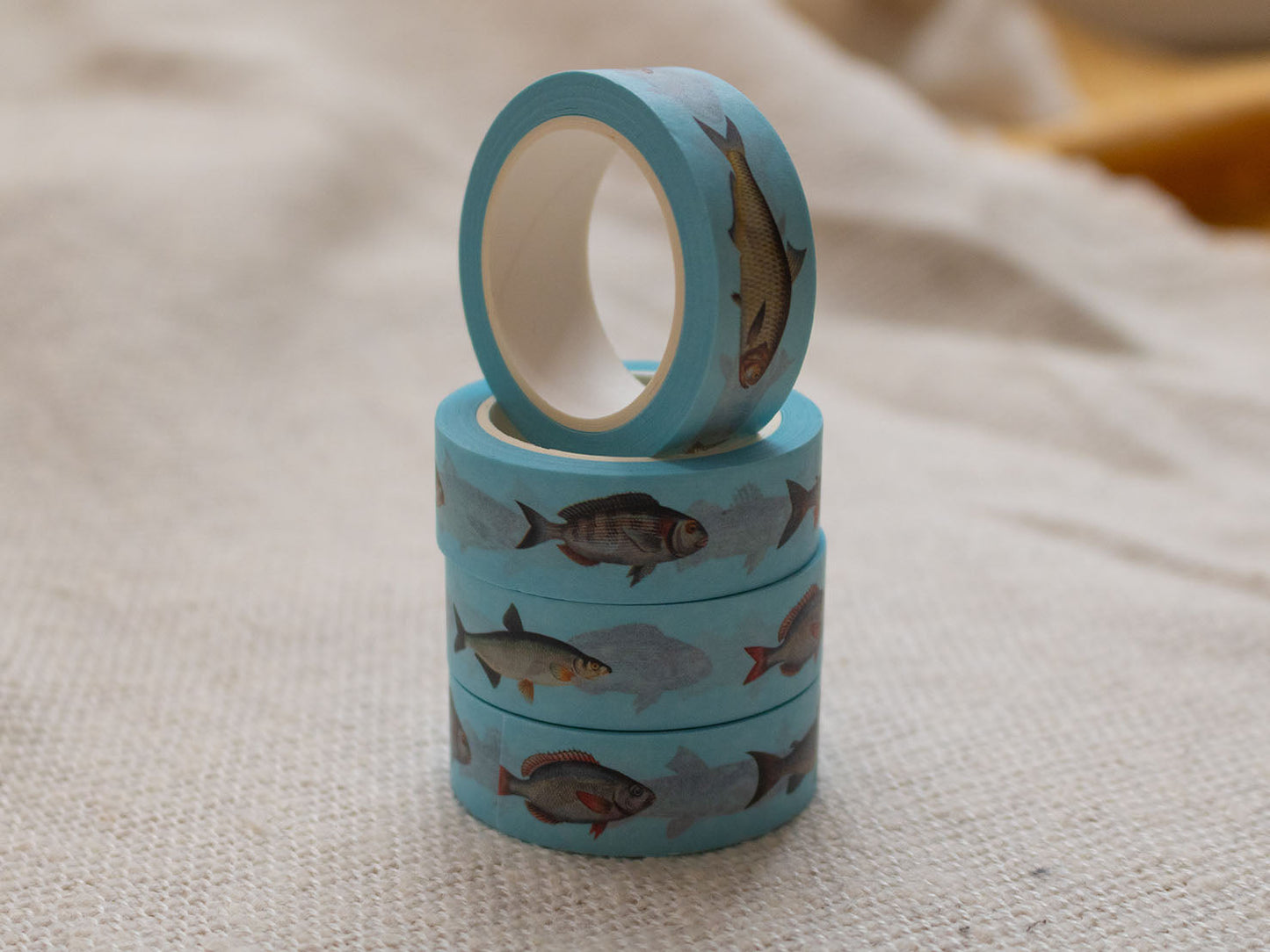 Stack of blue washi tape with fish design on a textured beige surface