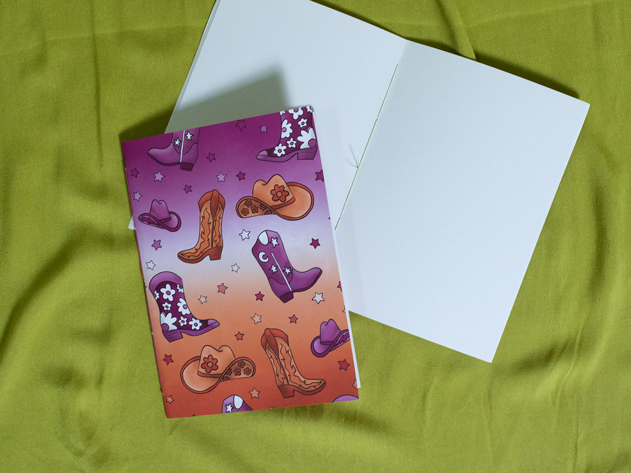 Sketchbook with cowboy boot and hat design on a green fabric background