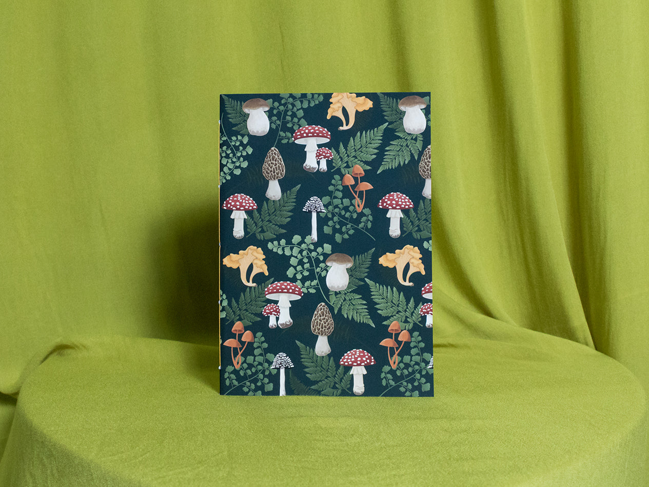 Sketchbook with a nature-themed design featuring mushrooms and plants on a green fabric background