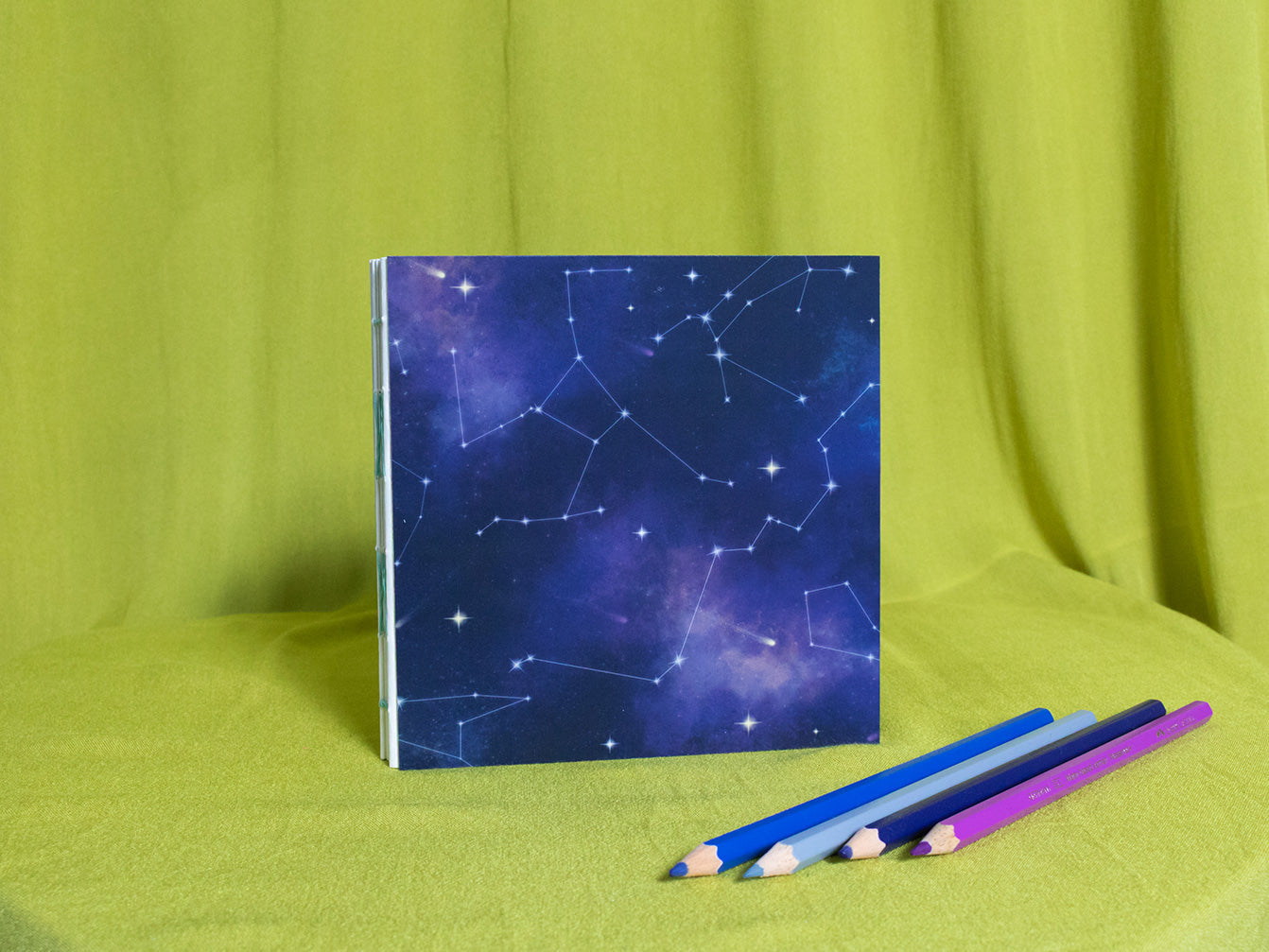 Square sketchbook with starry night design on a green fabric background
