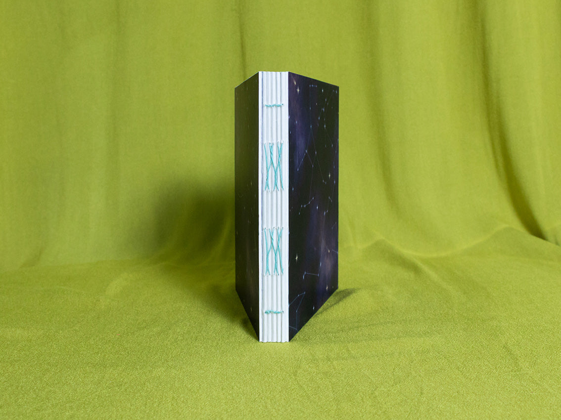 Open spine square sketchbook with cosmic pattern on a green fabric background