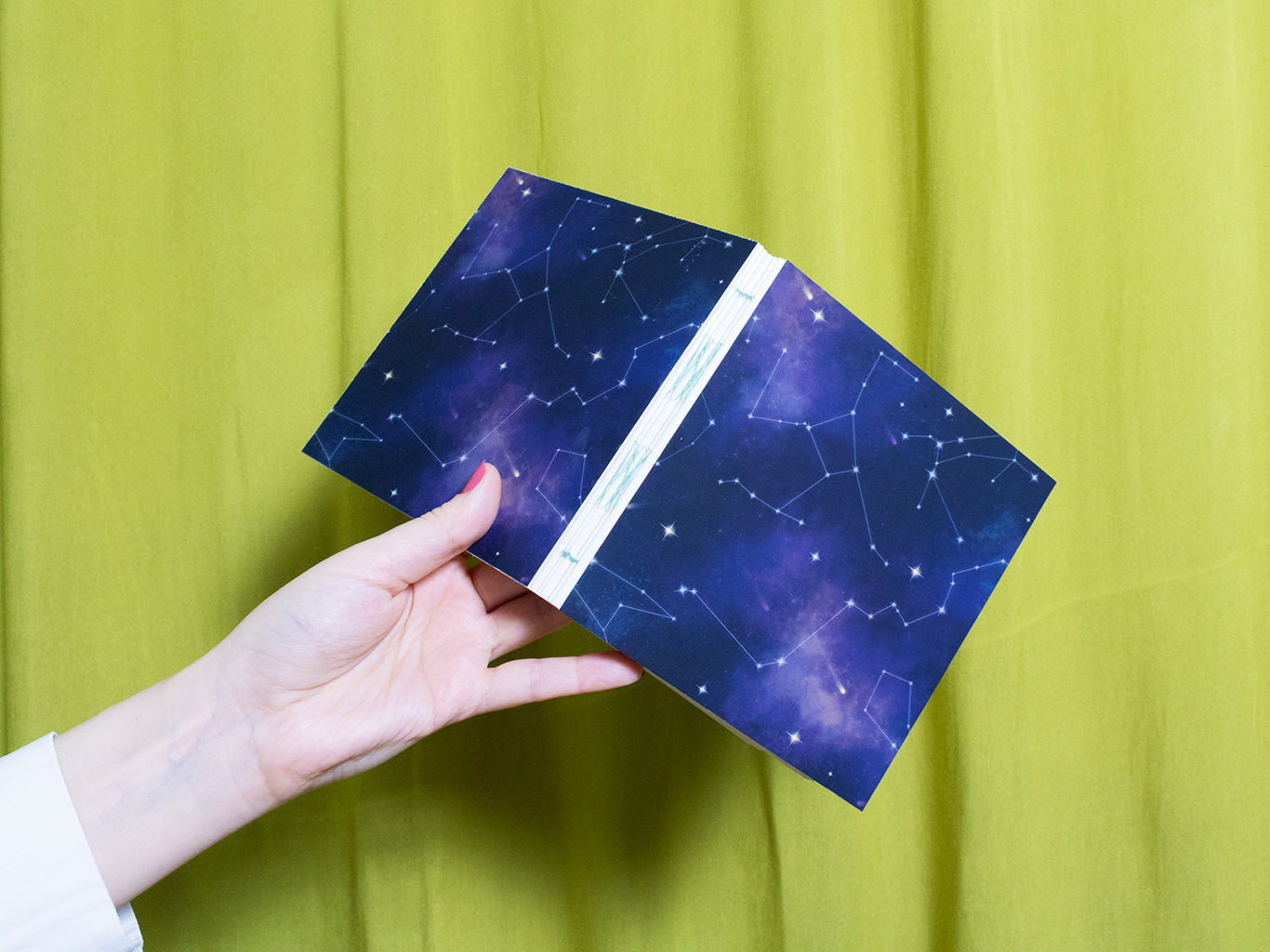 Hand holding a blue square sketchbook with star pattern against a green curtain background