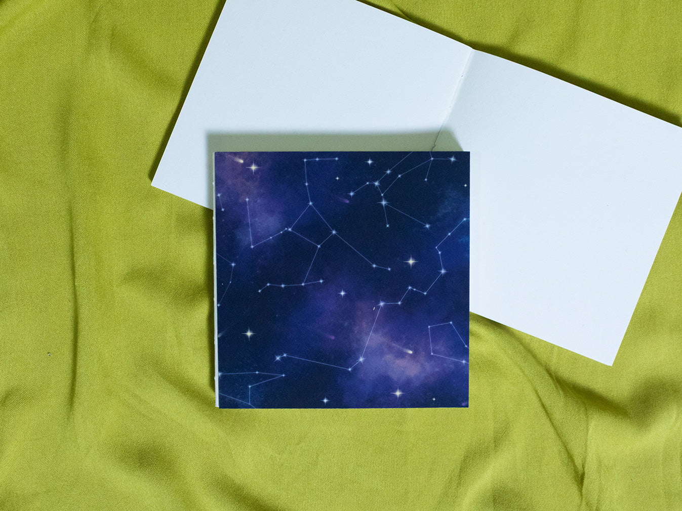 Square sketchbook with star constellation design on a green fabric background
