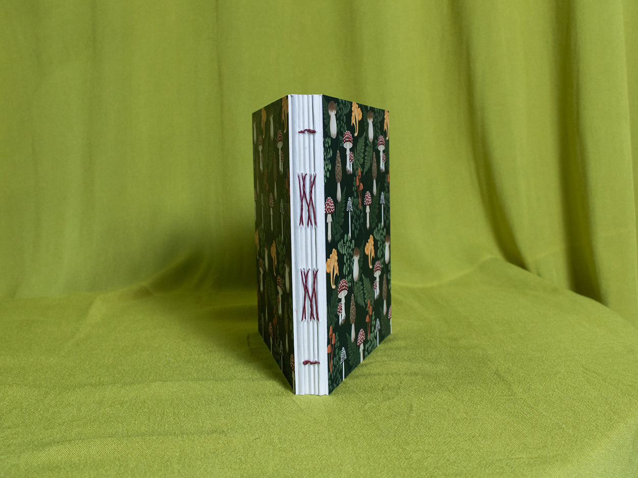Open spine sketchbook with decorative mushroom pattern cover on a green fabric background