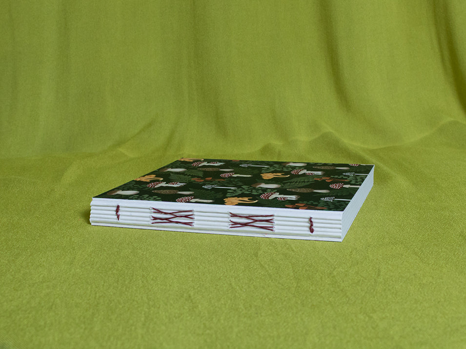 Square sketchbook with a green mushroom cover on a green fabric background