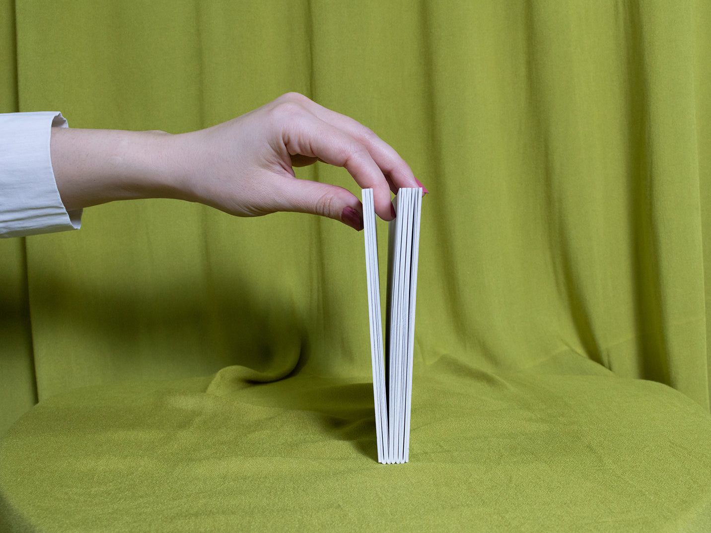 Hand holding a sketchbook sideways against a green fabric background